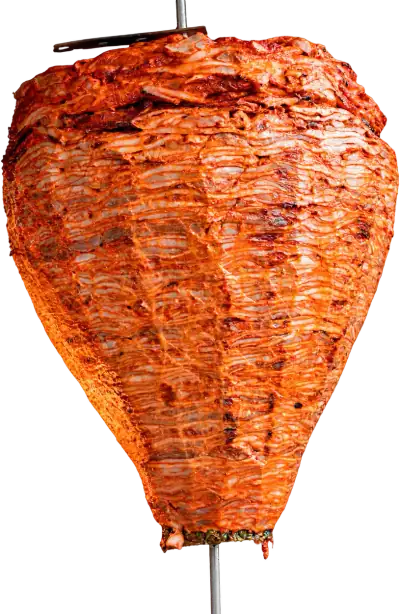 Trompo de pastor en el asador, con las capas de carne marcadas por el fuego y la piña en la base
