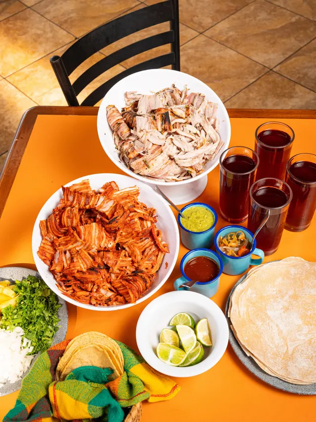Mesa con kilos de pastor, tortillas y salsas para taquiza