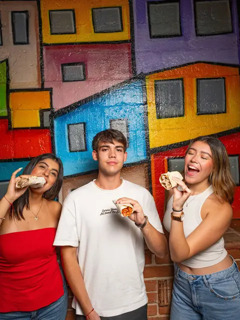 Tres clientes comiendo tacos frente al mural de la vecindad