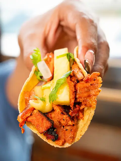 Taco de pastor con aguacate sostenido en la mano
